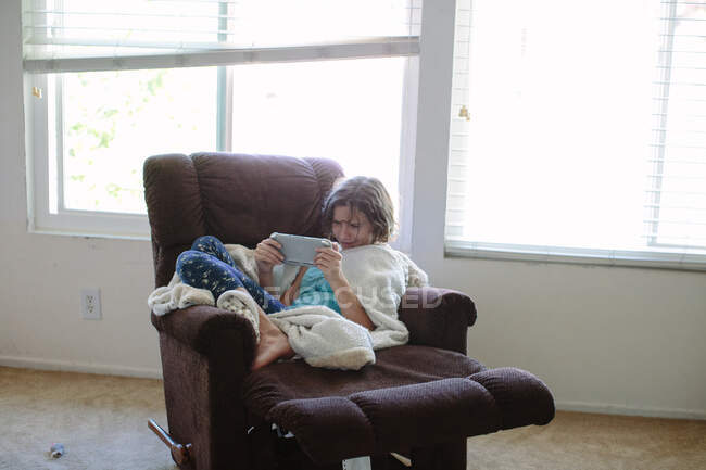 Menina adolescente em um reclinável joga jogos de vídeo em seu dispositivo de mão — Fotografia de Stock