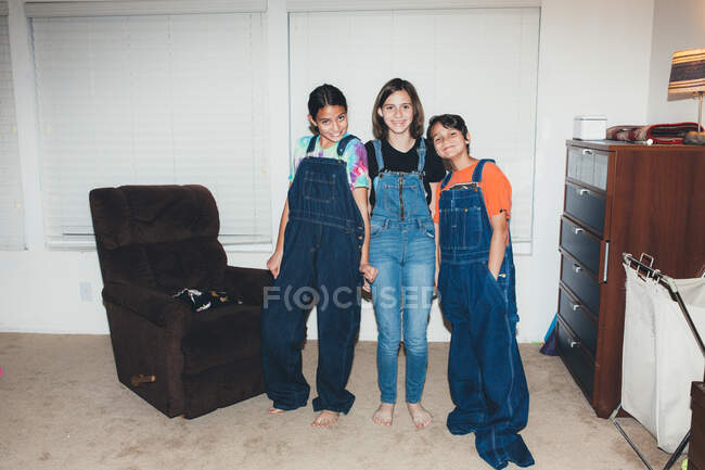 Three siblings smile while all wearing overalls and two oversized — Stock Photo