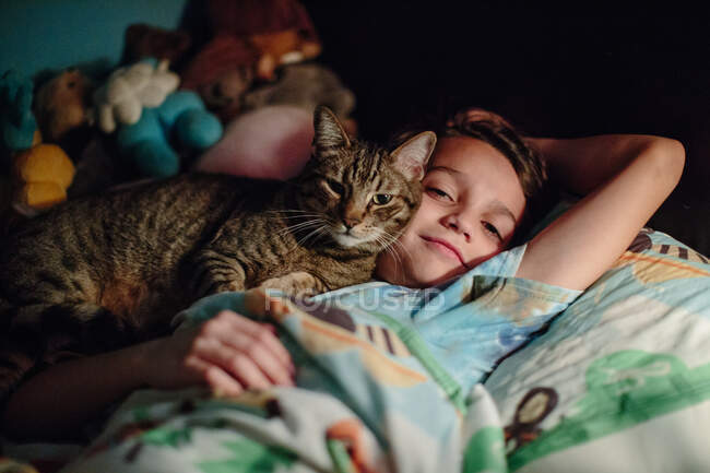 Niño y su gato tabby acurrucarse mejilla a mejilla en la cama - foto de stock