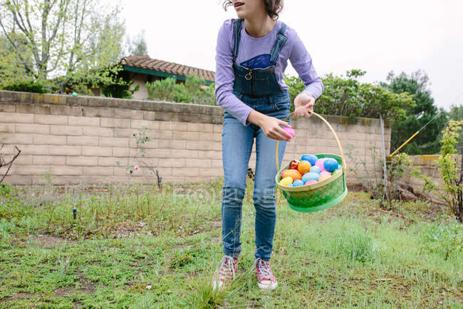 Девочка-подросток собирает пластиковые яйца на Пасху, чтобы положить в корзину — стоковое фото