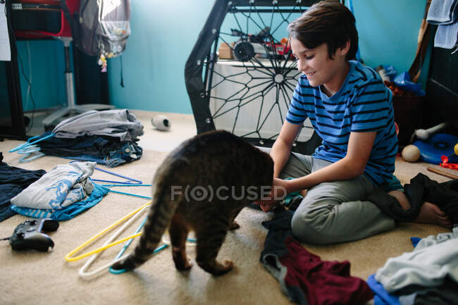 Niño de diez años sonríe mientras su gato lo distrae de sus tareas - foto de stock