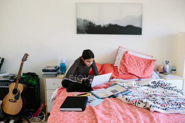 Menina do ensino médio senta-se com seu gato enquanto a aprendizagem on-line em sua cama — Fotografia de Stock