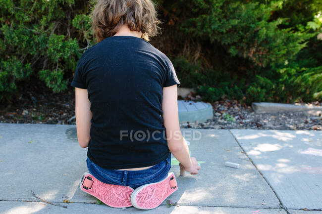 Der Rücken eines Mädchens, das auf dem Bürgersteig sitzt und Schuhe mit Rädern trägt — Stockfoto