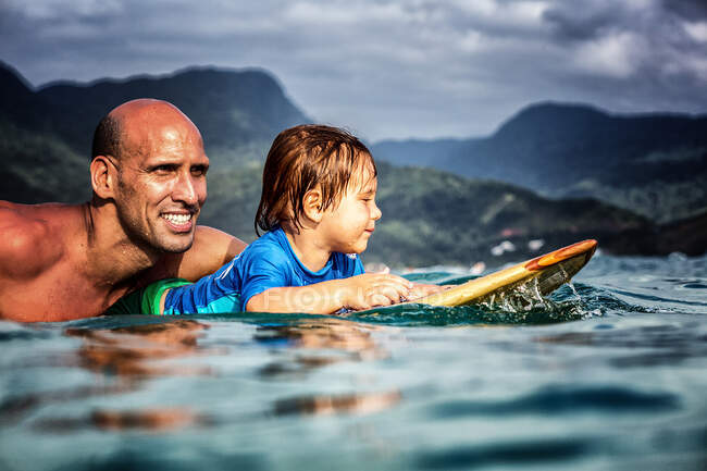 Padre y sol de 3 años remando en una tabla de surf de madera - foto de stock
