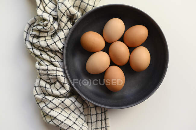 Oeufs de poulet dans un bol noir avec chiffon, vue sur le dessus — Photo de stock
