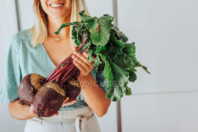 Молодая женщина держит свеклу с зелеными листьями и улыбается — стоковое фото