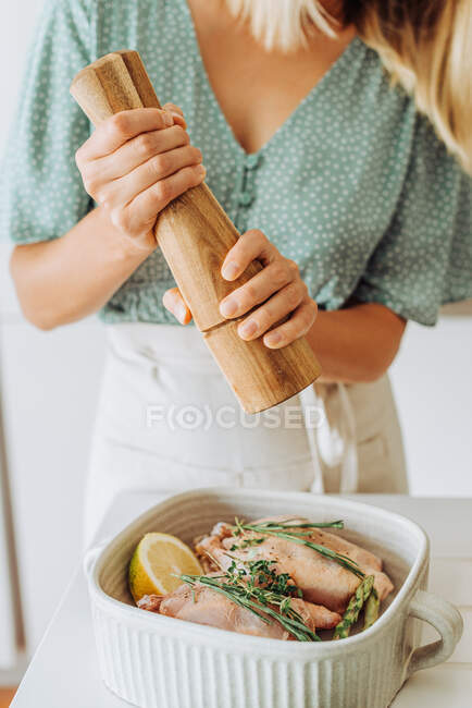 Jovem mulher europeia moendo pimenta na bandeja com codorniz para assar — Fotografia de Stock