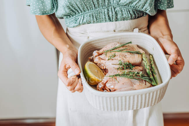 Young woman holding tray with raw chicken or quail with aromatic herbs — Stock Photo