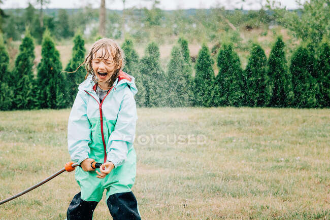 Girl laughing whilst playing with water in the yard at home — Stock Photo