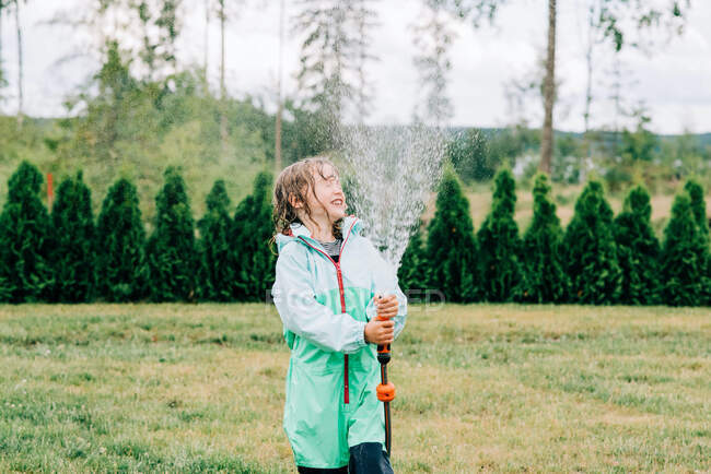 Девушка брызгает водой в лицо шлангом во дворе летом — стоковое фото