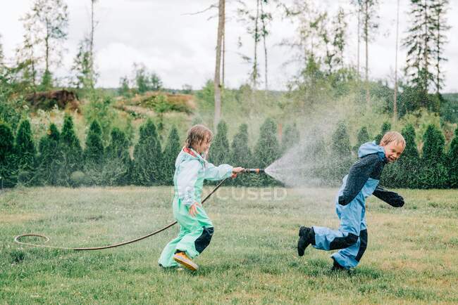 Irmão e irmã pulverizando uns aos outros com água no quintal em casa — Fotografia de Stock