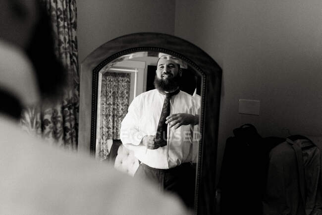 Retrato de un hombre mirándose en el espejo, poniéndose una corbata - foto de stock
