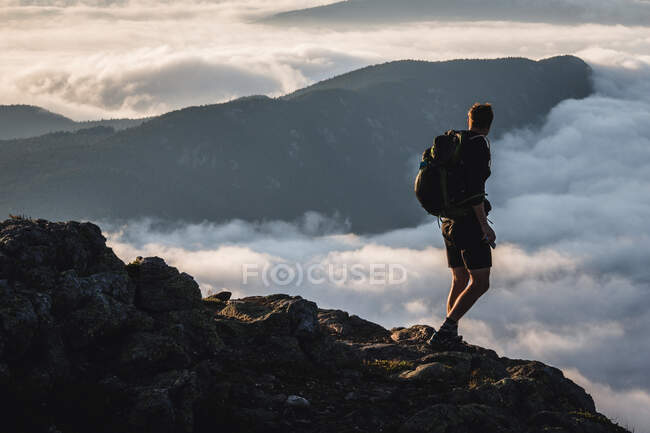 Männlicher Wanderer auf dem Gipfel blickt auf Berg, der über Wolken steigt, Maine — Stockfoto