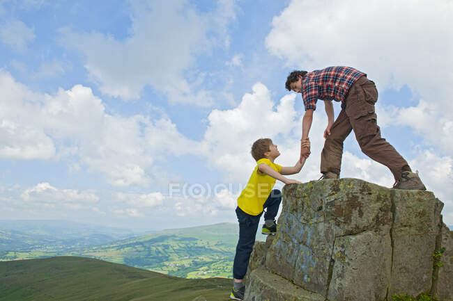 Teenage boy helping friend to climb rock — Stock Photo