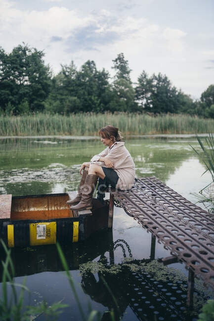 Женщина, сидящая на деревянном пирсе возле лодки — стоковое фото