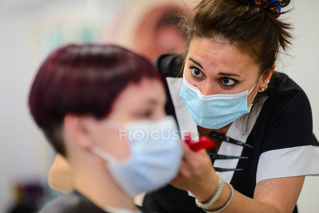 Female hair stylist at work wearing face mask while styling young girl — Stock Photo