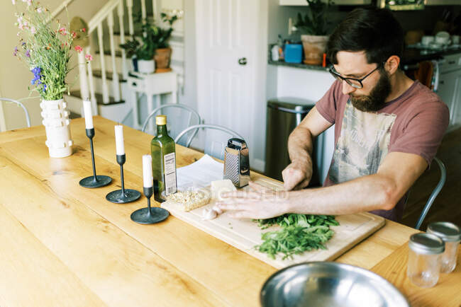 Um jovem cortando manjericão caseiro fresco para pesto caseiro — Fotografia de Stock