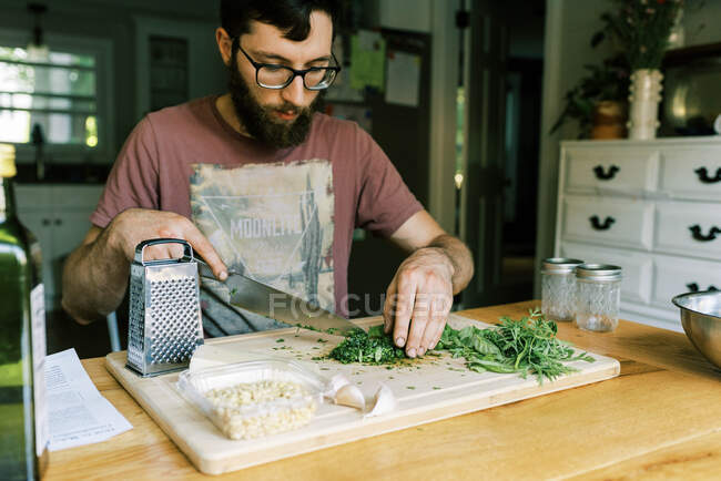 Ein junger Mann hackt frisches Basilikum für hausgemachtes Pesto — Stockfoto