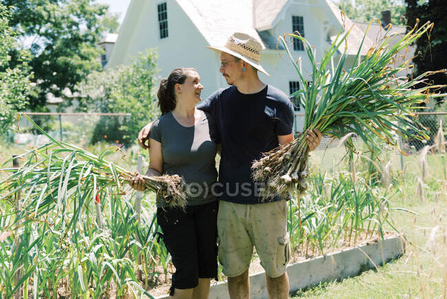 Portrait of a couple holding their freshly picked garlic bulbs — Stock Photo