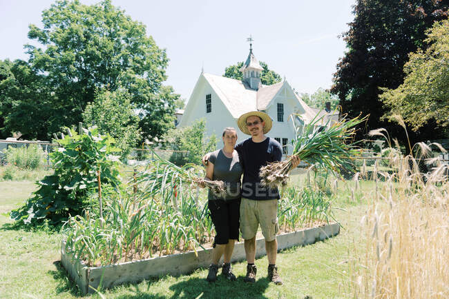 Retrato de una pareja sosteniendo sus bulbos de ajo recién recogidos - foto de stock