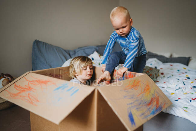 Niños varones jugando y dibujando en una caja durante el encierro - foto de stock
