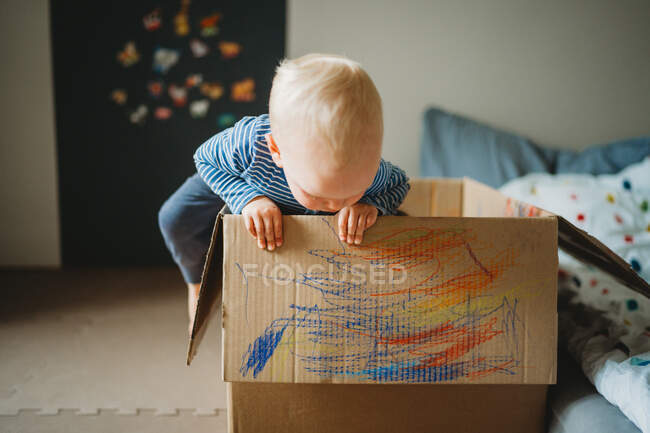 Jeune tout-petit jouant et dessinant dans une boîte à la maison pendant le confinement — Photo de stock