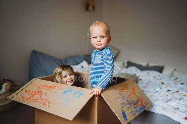 Hermanos jugando y dibujando en una caja durante el encierro - foto de stock