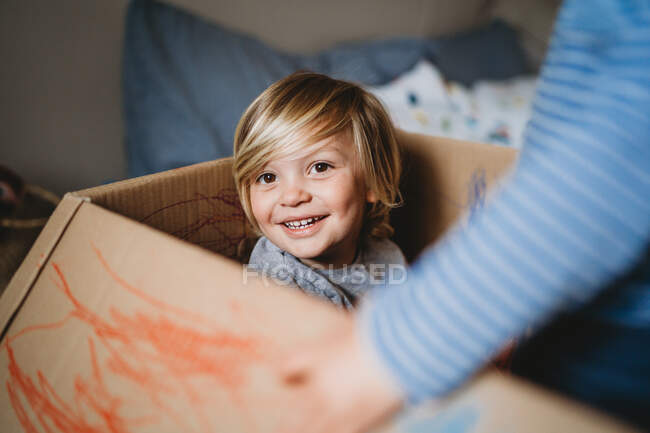 Jovem criança do sexo masculino sorrindo olhando para a câmera jogando em uma caixa — Fotografia de Stock