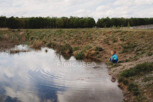 Enfant jouant avec un bâton dans l'eau dans un parc par une journée nuageuse — Photo de stock