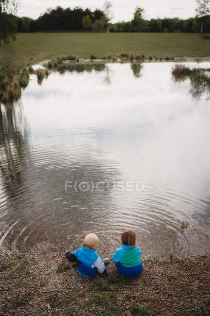 Vista trasera de los hermanos frente a un lago en un parque en un día nublado - foto de stock