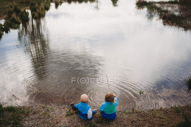 Back view of young kids in front of a lake in a park on cloudy day — Stock Photo