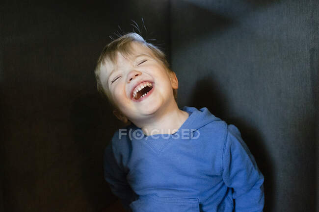 Joyful and happy toddler boy tilts head back while laughing indoors — Stock Photo