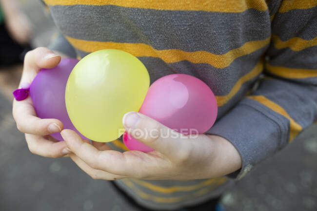 Ребенок в полосатой рубашке осторожно держит воздушные шары с водой в руках — стоковое фото