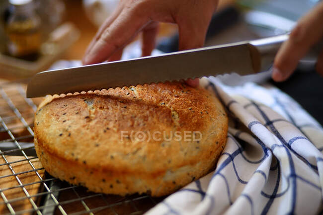 Hombre cortando pan casero horneado con cuchillo en la mesa - foto de stock