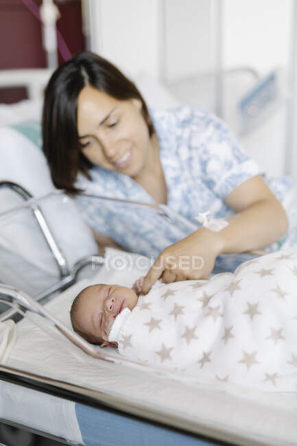 Cute newborn child sleeping and holding finger of happy mother in hospital — Stock Photo