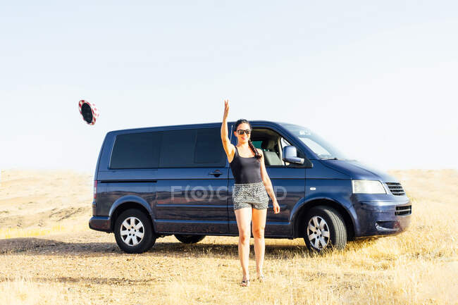 Uma jovem feliz em uma caravana em uma paisagem rural jogando seu chapéu — Fotografia de Stock