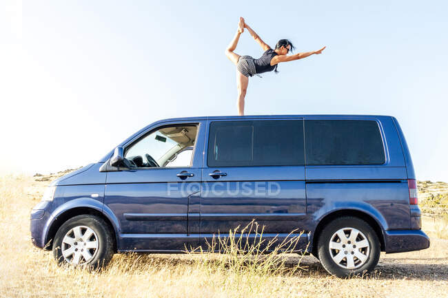 Eine Frau praktiziert Yoga auf dem Dach eines Wohnwagens in einer ländlichen Landschaft. — Stockfoto
