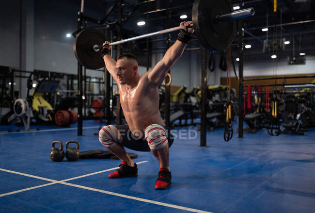 Full body shirtless athlete doing snatch exercise during intense training in gym — Stock Photo