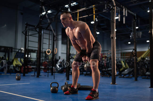 Corps entier athlète forte kettlebell balançant pendant l'entraînement intense dans la salle de gym — Photo de stock