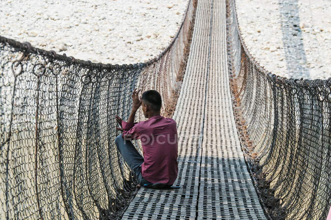 Человек, сидящий на подвесном мосту в Азии — стоковое фото