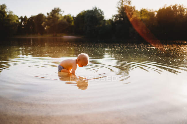 Male toddler looking for stones underwater at lake with reflection — Stock Photo
