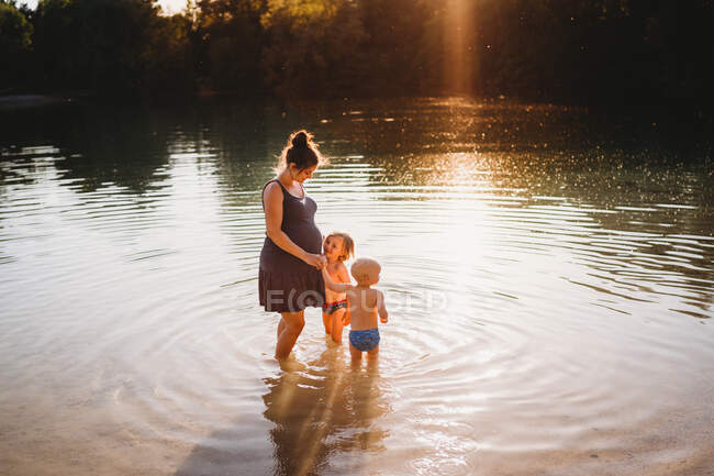 Вагітна жінка з дітьми в озері з золотим світлом. — стокове фото