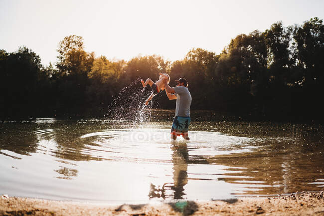 Father holding young child in the air at the lake splashing water — Stock Photo