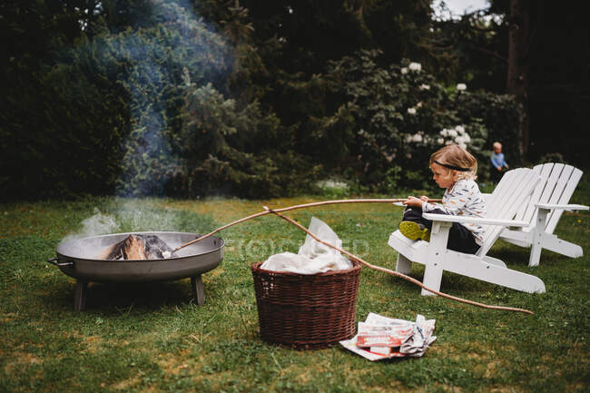 Біла дитина, яка тримає палицю сидячи на стільці, робить дим у багатті. — стокове фото