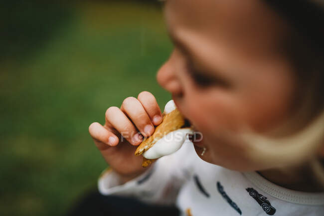 Close up detail of child's hand eating smores with melted marshmallow — Stock Photo