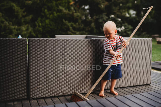 Young male child barefoot sweeping backyard patio with big broom — Stock Photo