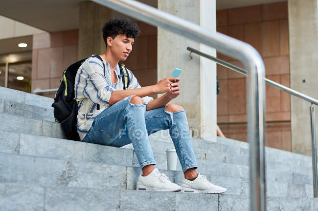 Young afro uses his mobile while he is sitting on the stairs — Stock Photo