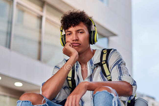 Aborrecido jovem afro com fones de ouvido em sentado na rua — Fotografia de Stock