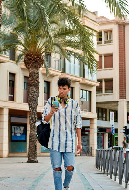 Young afro-haired man is walking down the street looking at his — Stock Photo