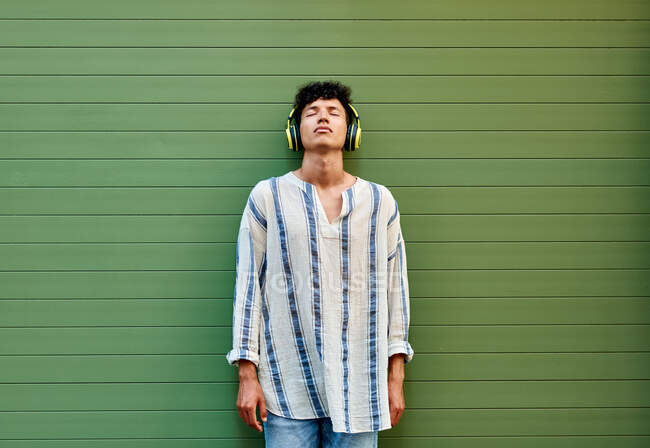 A young Afro-haired man listens to music on a green background — Stock Photo